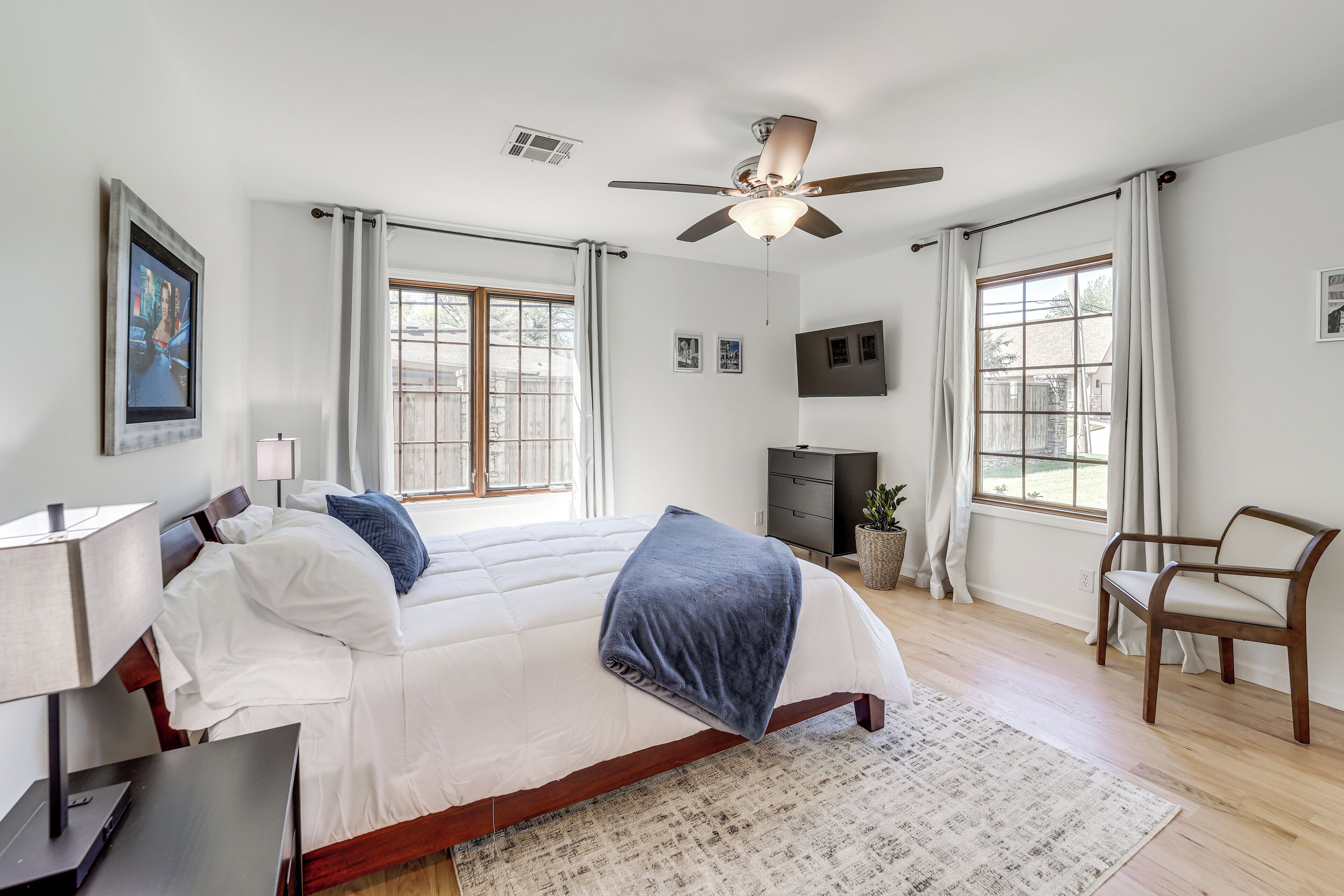 A bedroom with a bed, a desk, a chair, a ceiling fan, and a window.