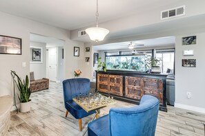 Ein Wohnzimmer mit einem Schachbrett, blauen Stühlen, einer Holzkommode und einem großen Fenster.