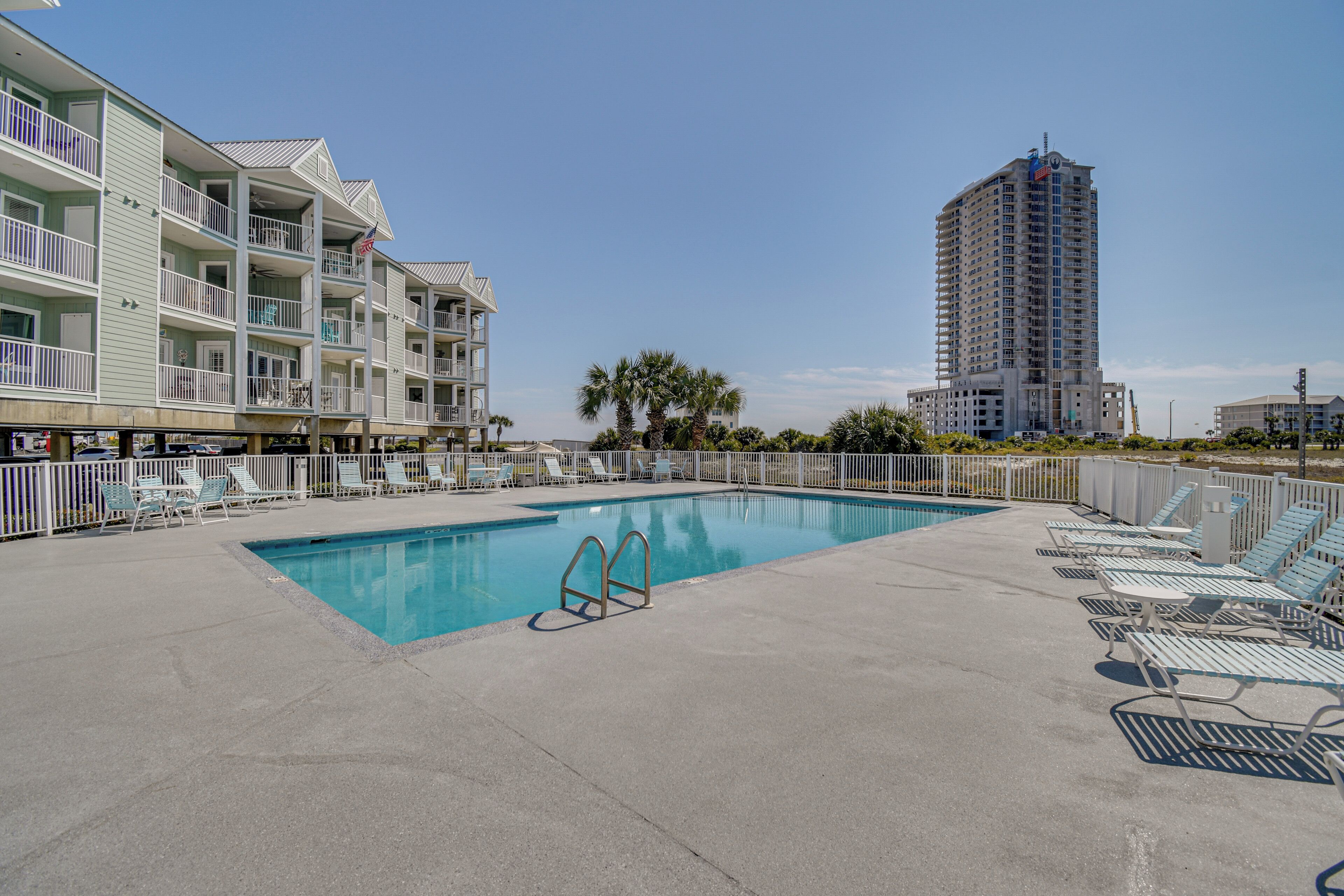 A swimming pool with lounge chairs, a building with balconies, and a tall skyscraper in the background.