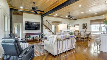 A spacious living room with a sofa, a black leather chair, a dining area with a table and chairs, a staircase, and a kitchen area.