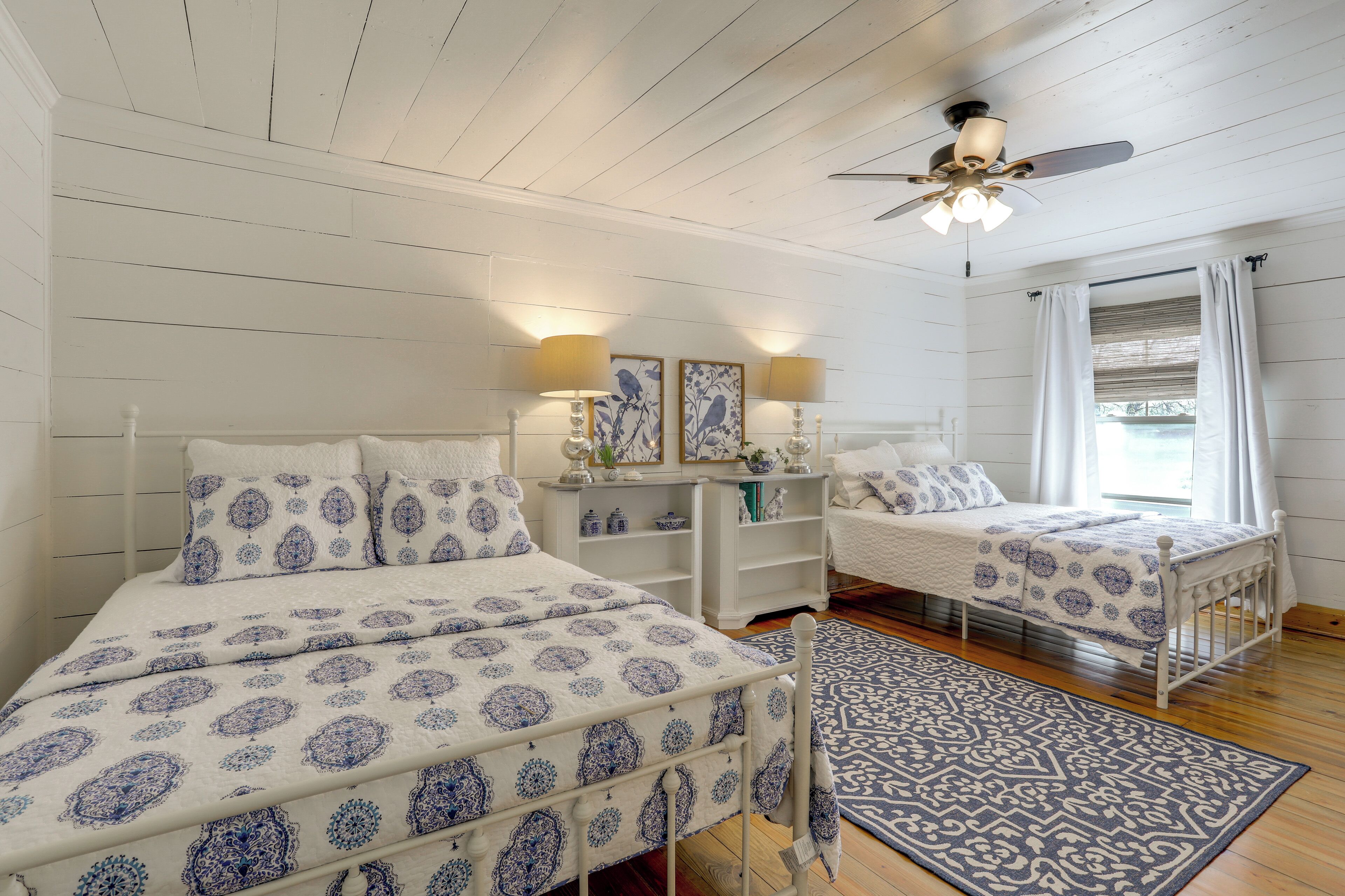 A bedroom with two beds, a ceiling fan, bedside lamps, and a window with curtains.