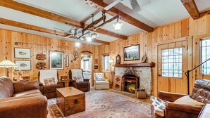 A log cabin interior with a fireplace, leather furniture, wooden walls, and a large rug. - Gateway to Sequoia Natl! Rustic Cabin w/ Patio (Camp Nelson)