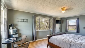 Quarto com cama, escrivaninha com cadeira, micro-ondas e janela.