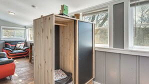 Ein Zimmer mit einem Holzkasten, einem roten Sofa und einem Fenster mit Blick auf Bäume.