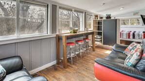 Eine Küche mit Barbereich, Holzstühlen, einer Couch und Blick durch große Fenster.