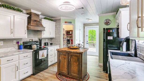 A kitchen with white cabinets, a wooden island, a black refrigerator, and a microwave. - Explore Tupelo & Natchez Trace! Southern Getaway (Tupelo)