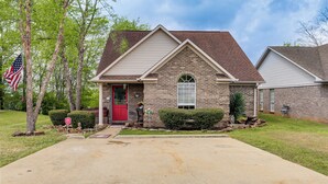 A two-story house with a red door, a brick exterior, and a front yard with a flag and a mailbox. - Explore Tupelo & Natchez Trace! Southern Getaway (Tupelo)