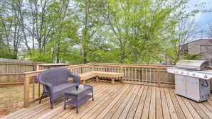 A wooden deck with a grill, a bench, and a wicker chair. - Explore Tupelo & Natchez Trace! Southern Getaway (Tupelo)
