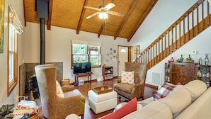 A spacious living room with a high ceiling, wooden beams, a fireplace, a television, and a staircase. - Pets Welcome! Quiet Retreat w/ Covered Back Deck! (Dahlonega)