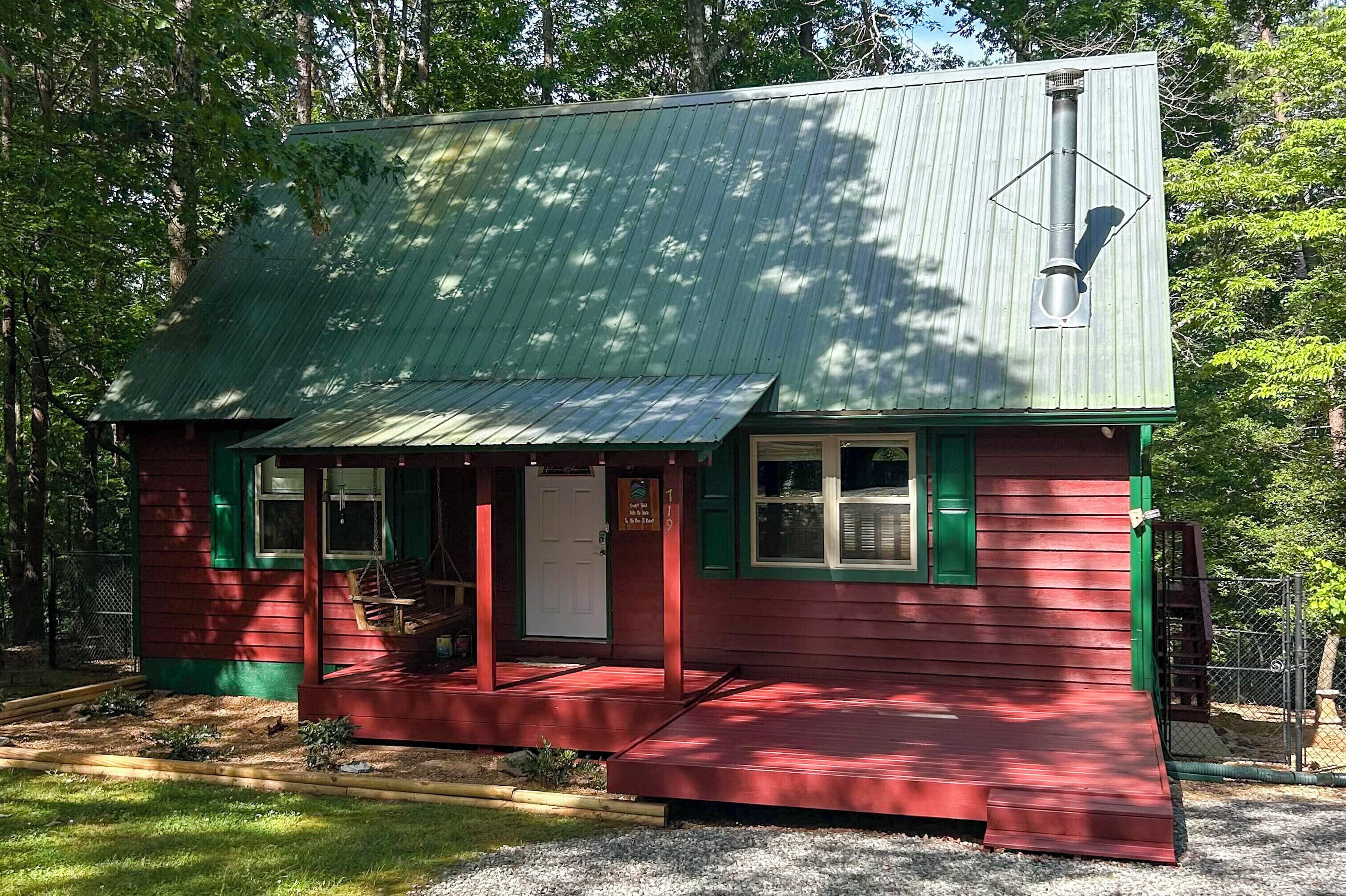 A small, red wooden building with a green roof, a porch, and a door.