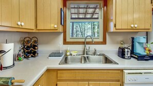 A kitchen with wooden cabinets, a stainless steel sink, a window with a view of trees, a toaster, and a coffee maker. - Pets Welcome! Quiet Retreat w/ Covered Back Deck! (Dahlonega)