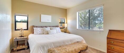 A bedroom with a bed, bedside lamps, a dresser, a bench, and a window with blinds.