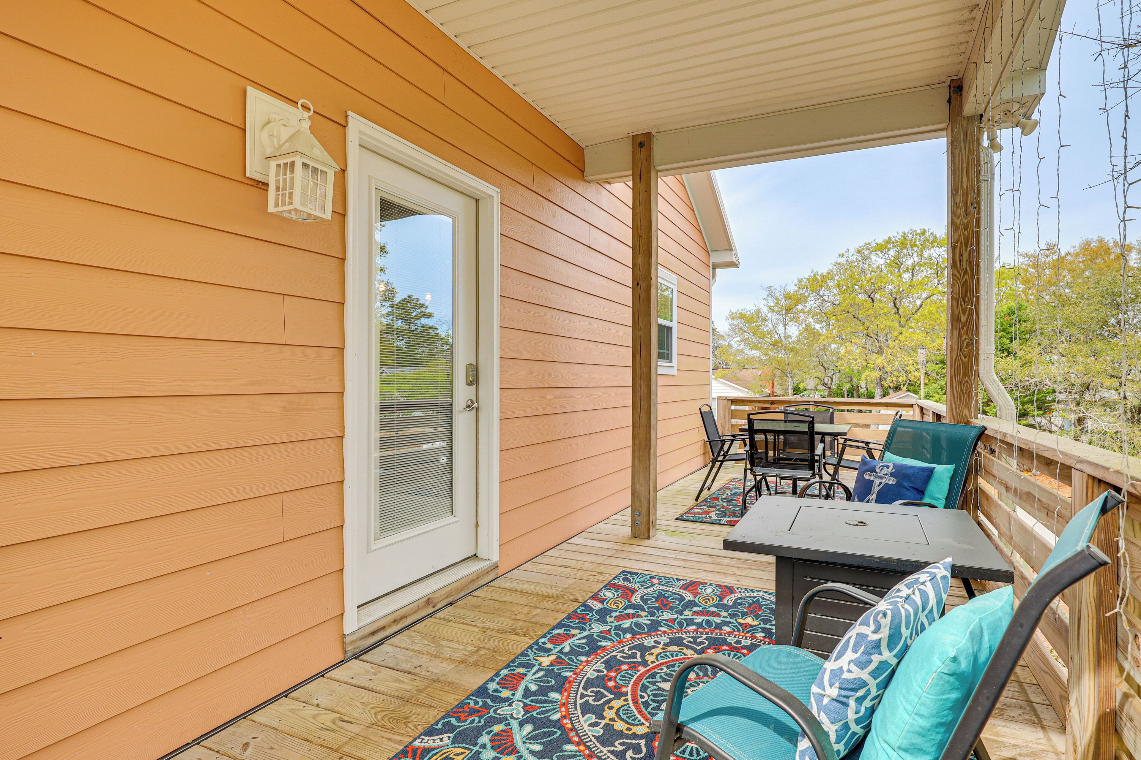 A covered outdoor patio with a table and chairs, a door, and a view of trees.