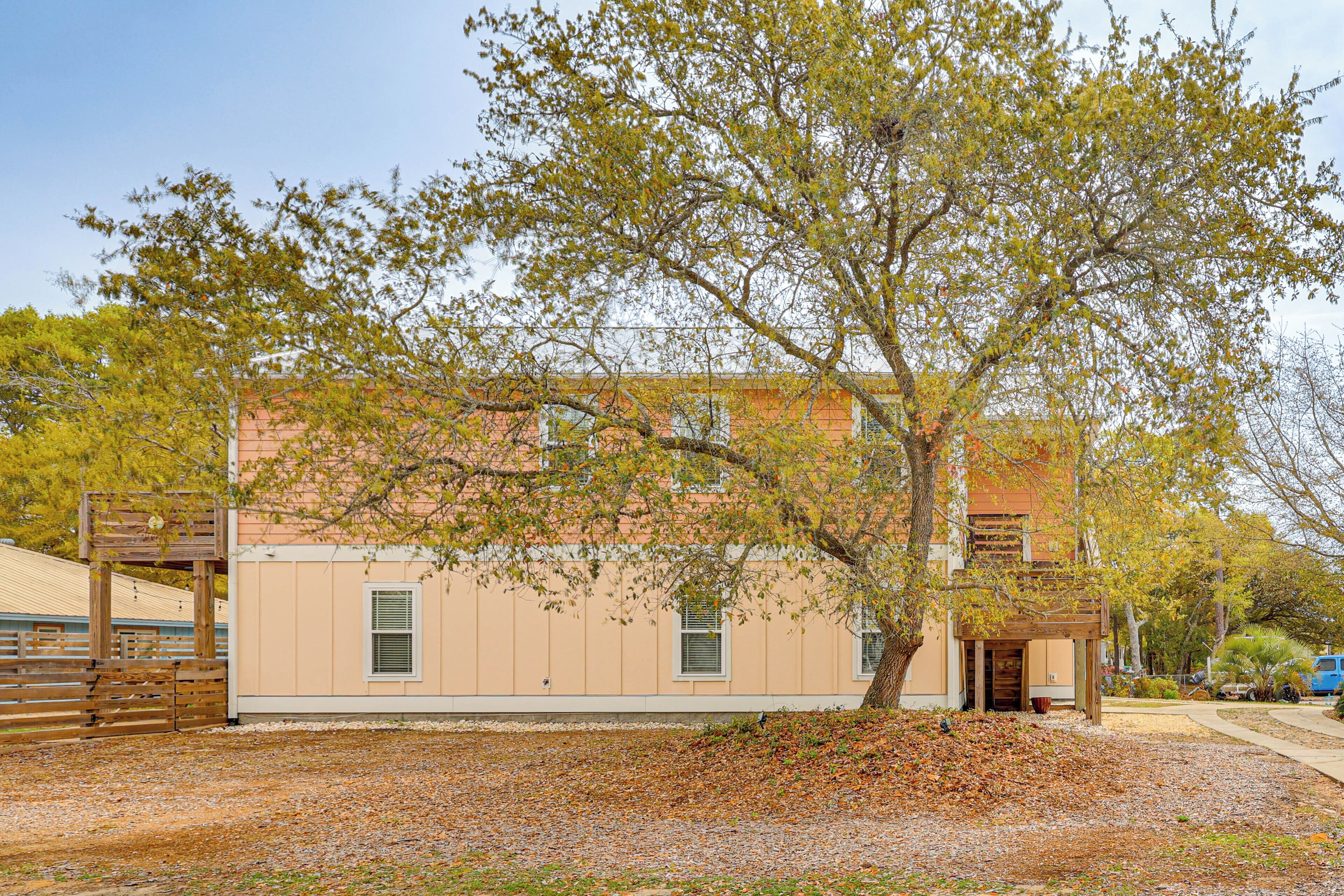 A building with a large tree in front, a fenced area, and a clear sky.