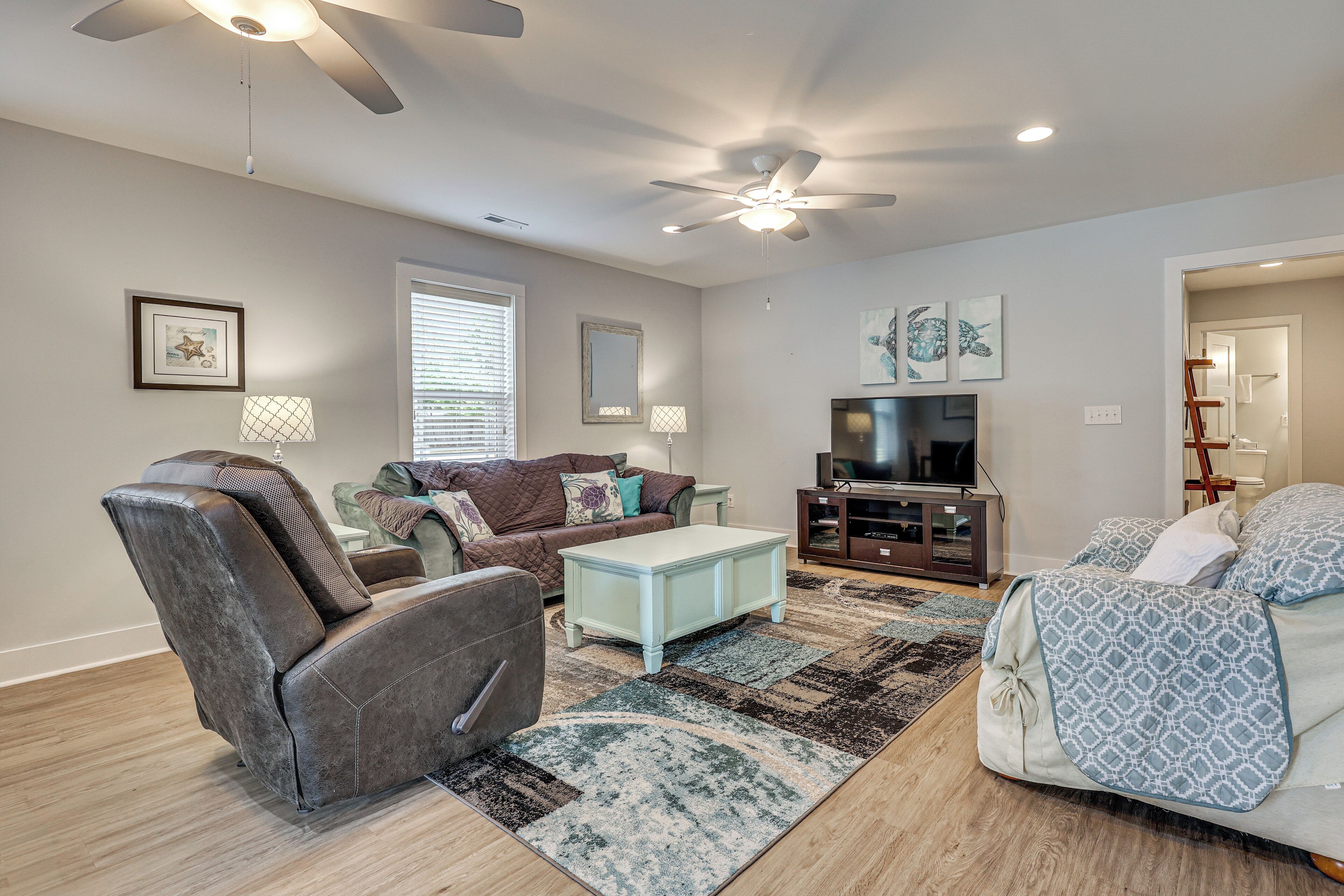 A living room with a ceiling fan, a TV, a sofa, a recliner, and a patterned rug.
