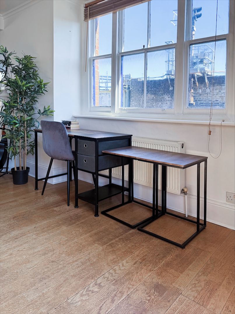 Una habitación con escritorio, silla, planta en maceta y ventana con vista a un edificio.