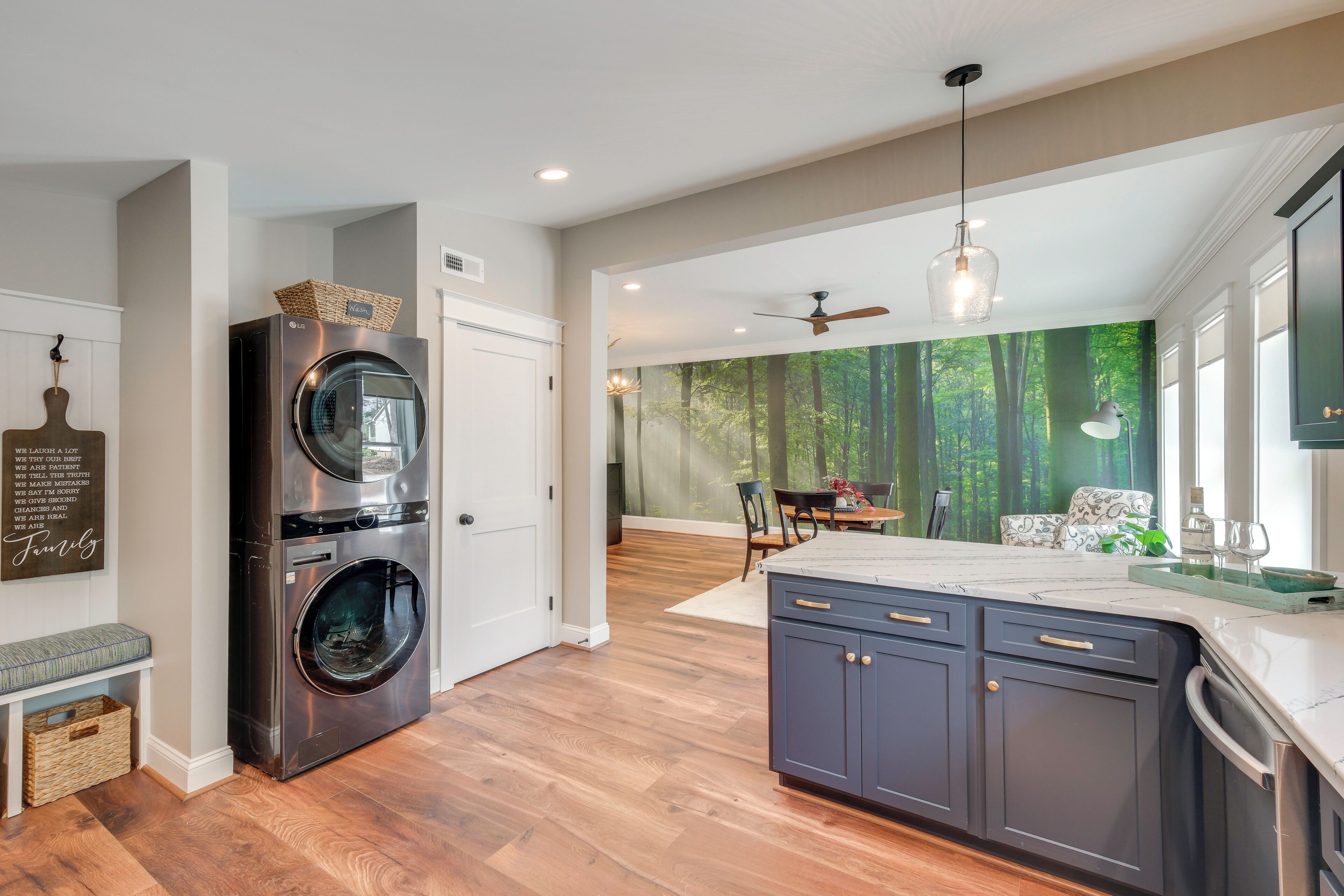 A modern kitchen with a built-in washer and dryer, a dining area with a view of the forest, and a large island with dark cabinetry.