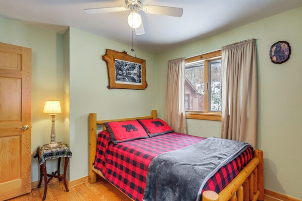 A bedroom with a bed, a ceiling fan, a window with curtains, a wooden door, and a small table with a lamp. - All-season Family Retreat w/ Dock on Loon Lake! (Chestertown)