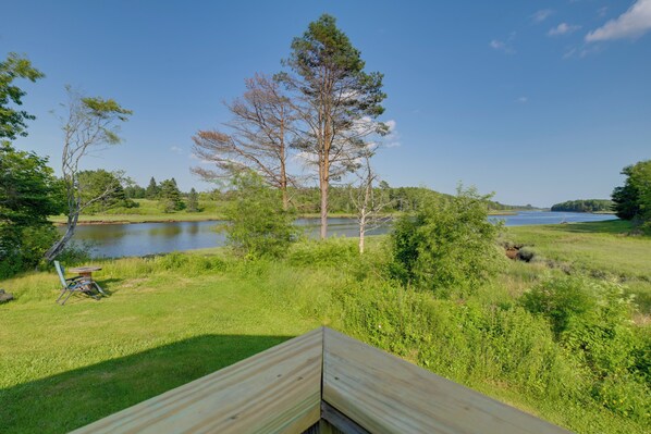 Blick auf ein Seeufer mit einer Holzterrasse, einem Tisch mit Stühlen und einer Bank.