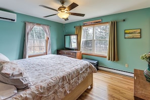 A bedroom with a bed, a ceiling fan, a dresser, a TV, and a window with curtains.