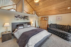 A bedroom with a large bed, a sofa, wooden ceiling beams, a fireplace, and a painting on the wall. - Fun w/ Family! Lakefront Gem in Jamestown (Jamestown)