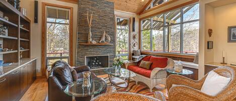 A spacious living area with a fireplace, wicker furniture, and large windows.