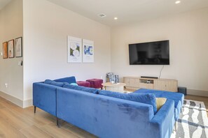 A living room with a blue sofa, a small round table, a TV mounted on the wall, and a wooden cabinet. - Walk to Lake Travis & Parks! Resort-style Getaway (Leander)