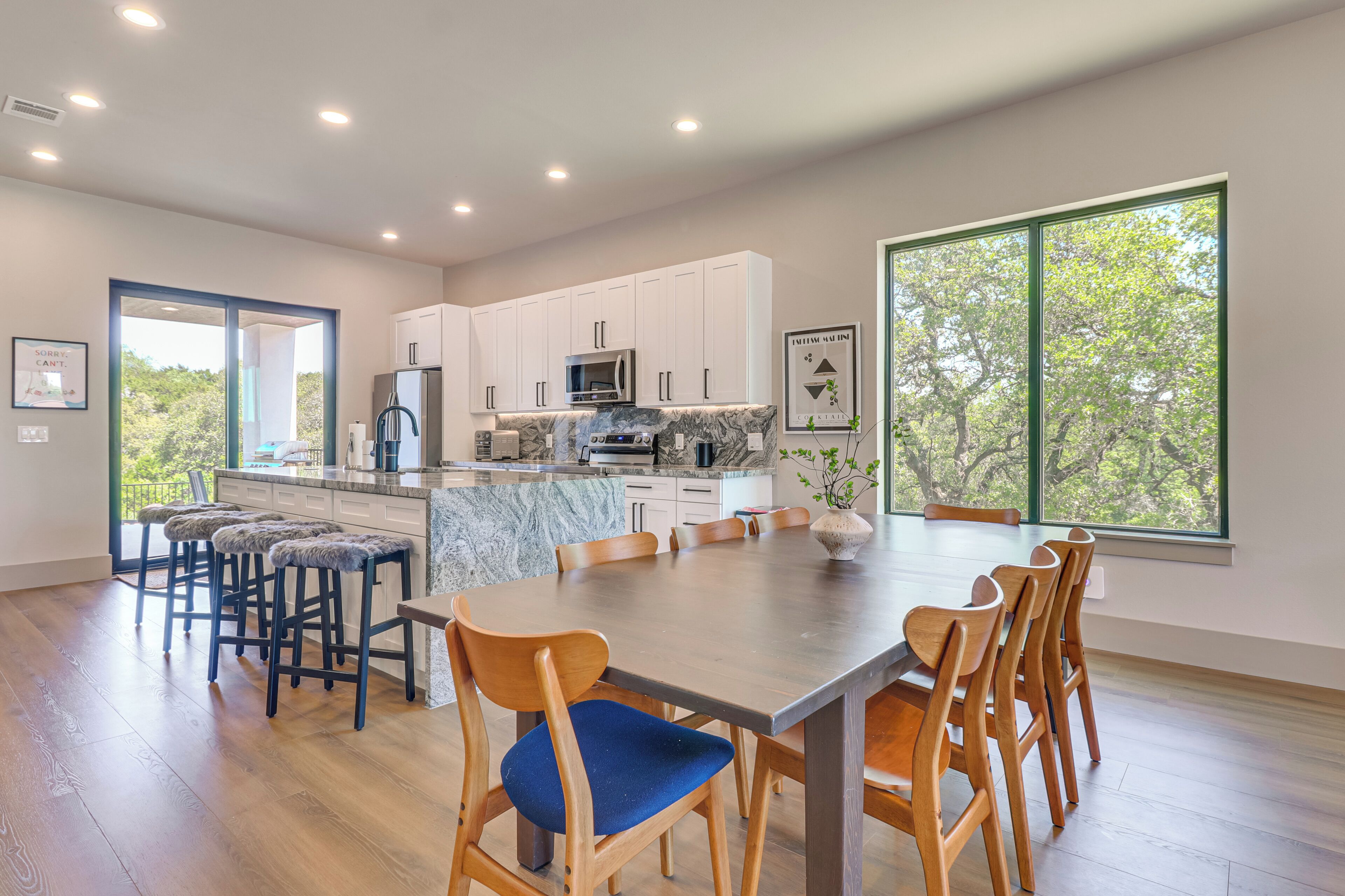 A modern kitchen with white cabinets, a marble island, and a dining area with wooden chairs and a large table.