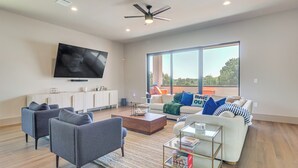 A modern living room with a flat-screen TV, two sofas, a coffee table, and a large window offering a view. - Walk to Lake Travis & Parks! Resort-style Getaway (Leander)