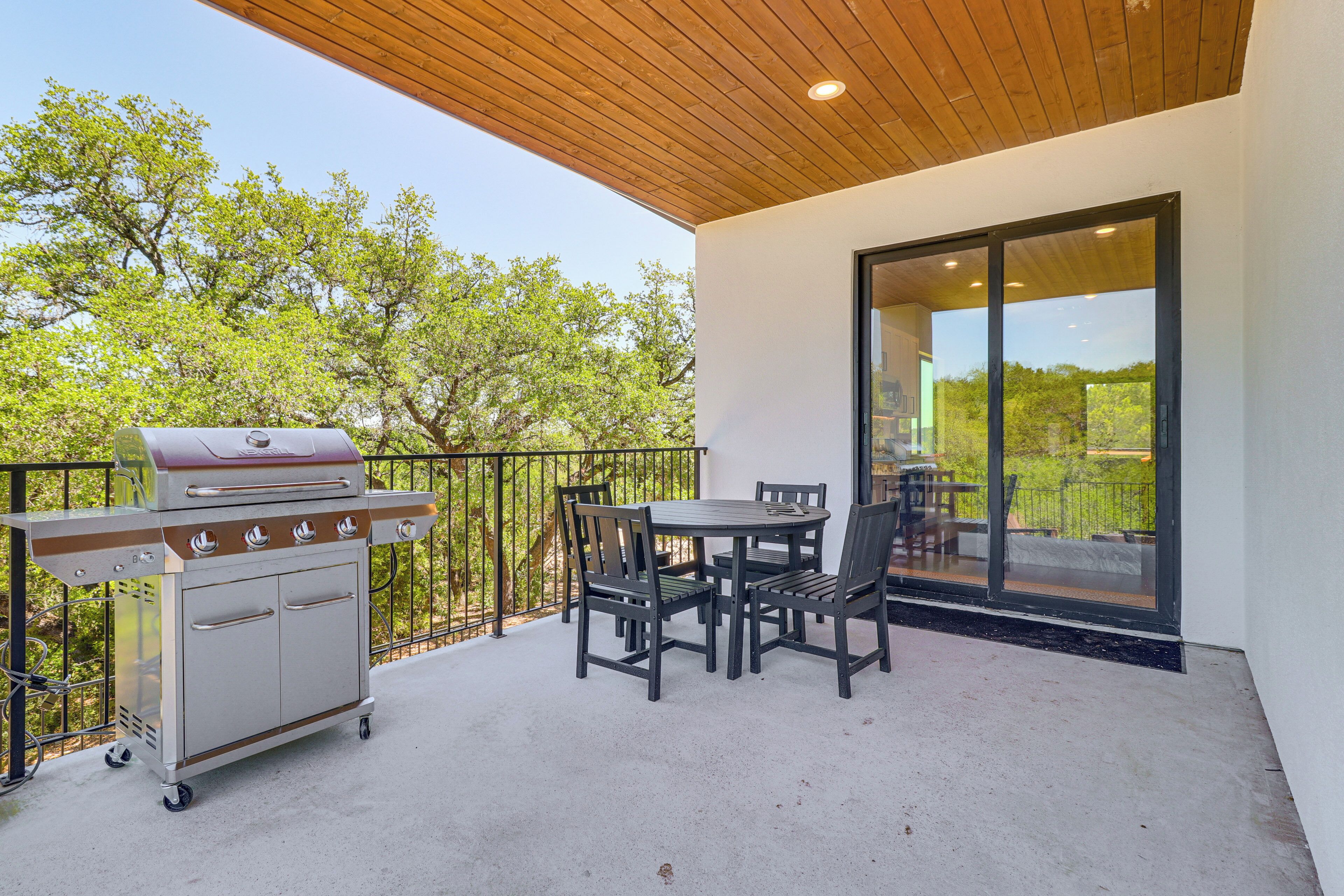 An outdoor patio with a grill, a table with chairs, and a glass door leading to a balcony.