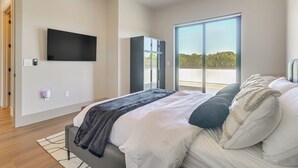 A modern bedroom with a bed, a flat-screen TV, a wardrobe, and a large sliding glass door to the outside. - Walk to Lake Travis & Parks! Resort-style Getaway (Leander)