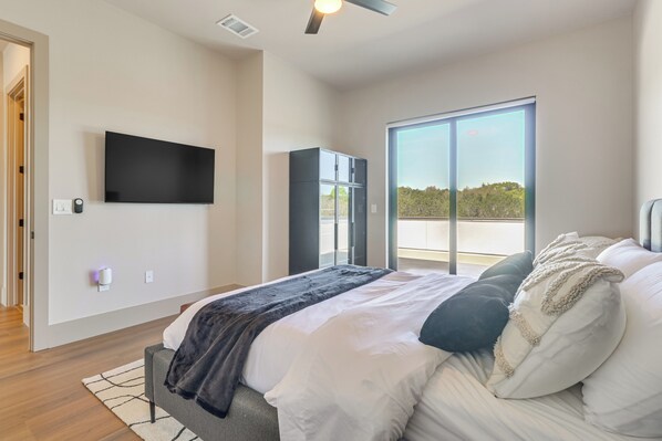 A modern bedroom with a bed, a flat-screen TV, a wardrobe, and a large sliding glass door to the outside. - Walk to Lake Travis & Parks! Resort-style Getaway (Leander)