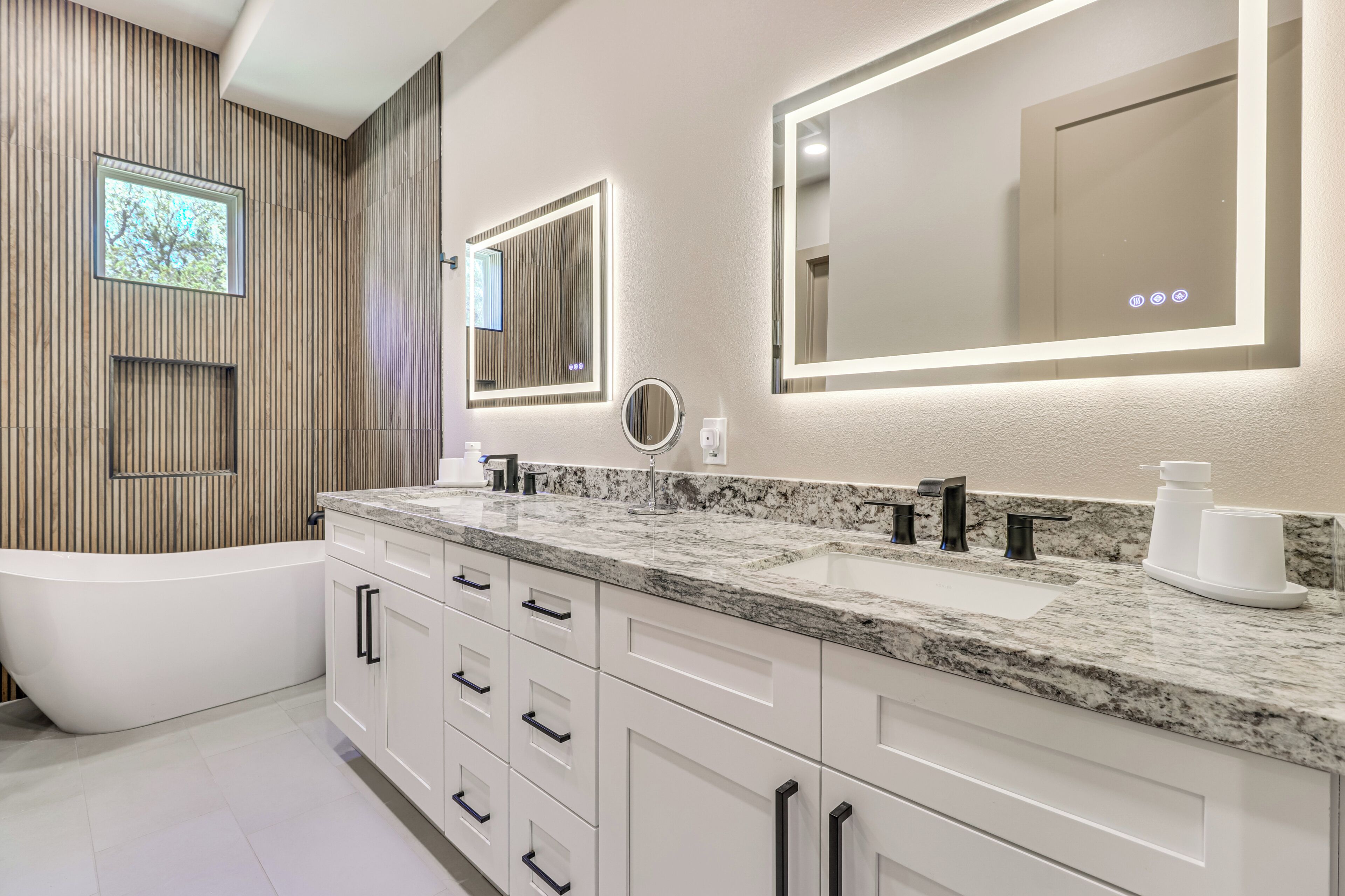 A modern bathroom with a freestanding bathtub, double sinks, and a large mirror with integrated lighting.