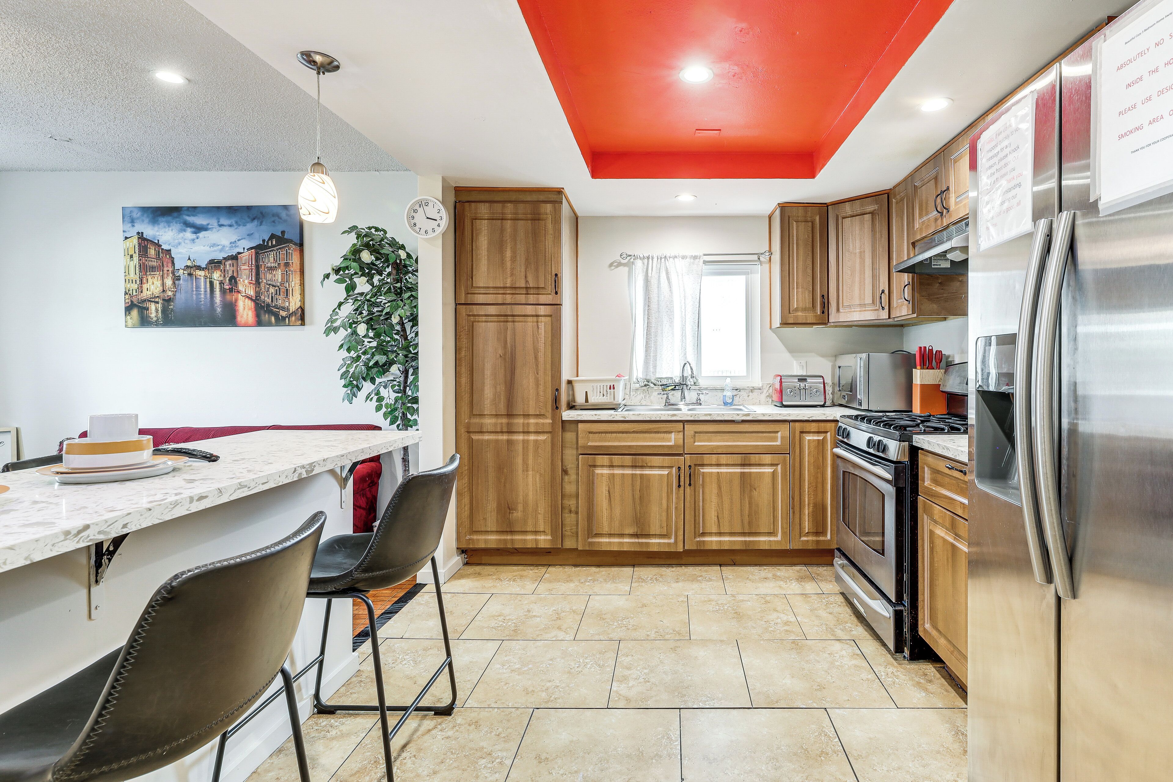 Una cocina moderna con armarios de madera, un refrigerador de acero inoxidable, una estufa y un comedor con encimera de mármol y sillas.