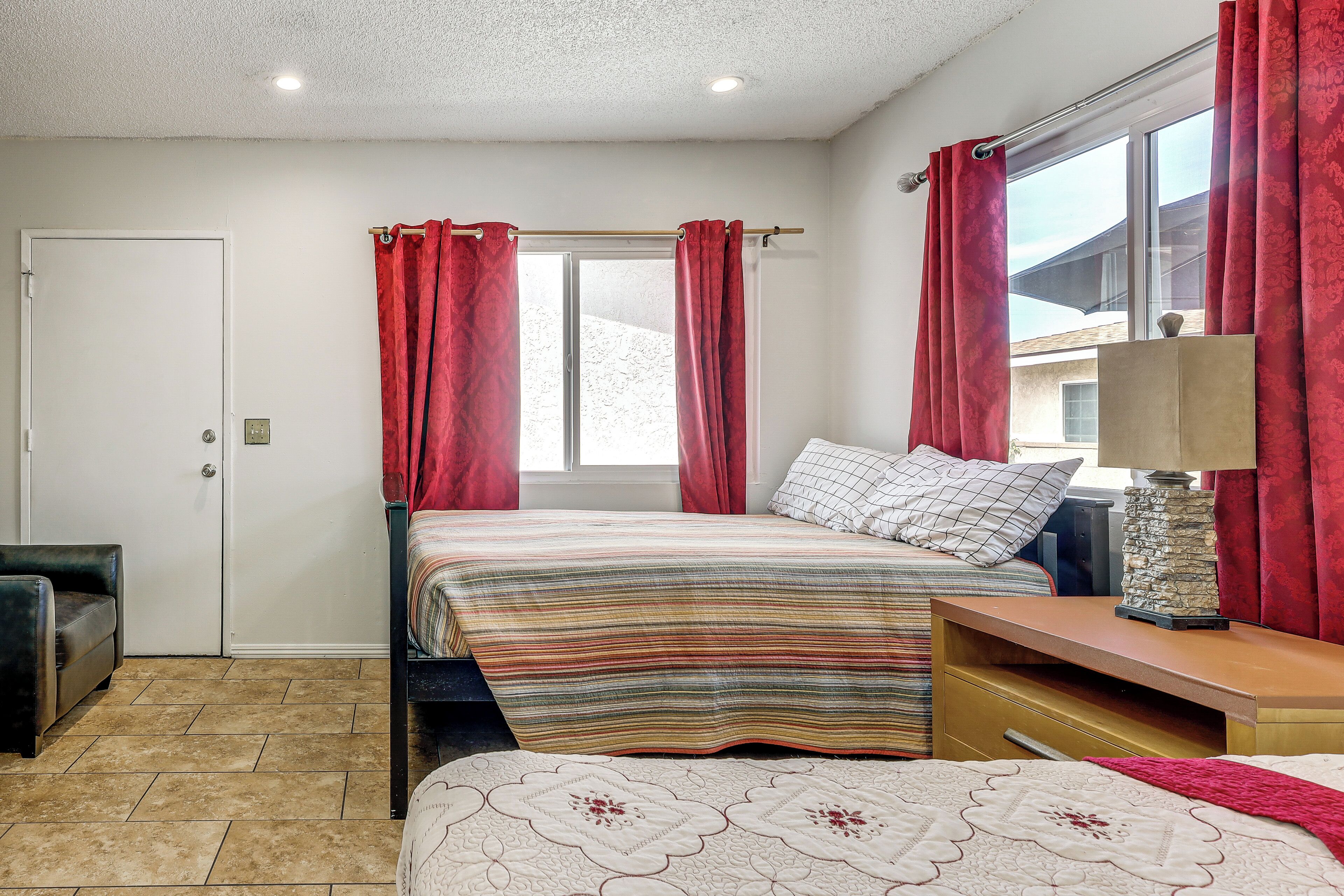 Un dormitorio con cama, una mesita de noche, una lámpara, una ventana con cortinas y una puerta.