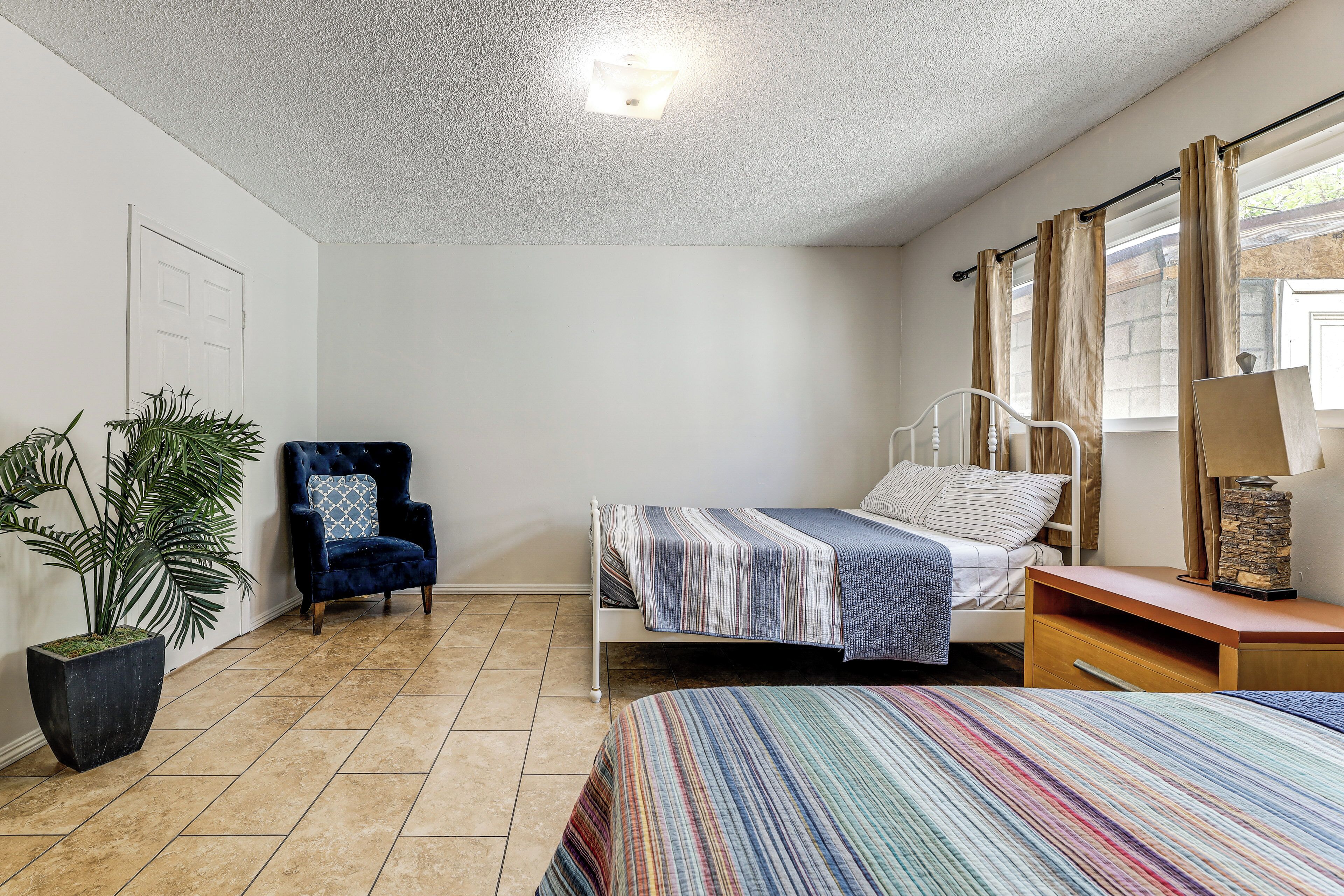 A bedroom with a bed, a chair, a nightstand, a lamp, and a potted plant.