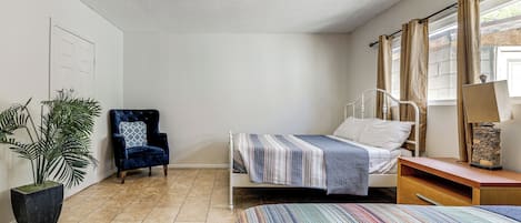 A bedroom with a bed, a chair, a nightstand, a lamp, and a potted plant.