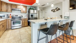 Una cocina con armarios de madera, electrodomésticos de acero inoxidable, encimera de mármol y una zona de bar con taburetes.