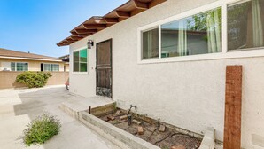 Un edificio residencial con entrada de hormigón, terraza de madera y pequeño jardín.