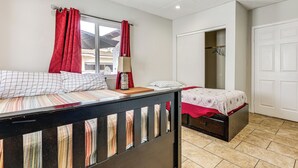 Un dormitorio con dos camas, una ventana con cortinas rojas, una mesita de noche con lámpara y un armario.