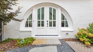 A white brick house with a symmetrical front door, a small garden with plants and gravel, and a clear sky. - Luxury home in Trilith steps from US Soccer Center, Pool, and Restaurants (Fayetteville)