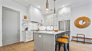 A modern kitchen with white cabinetry, a central island with stools, and pendant lighting. - Luxury home in Trilith steps from US Soccer Center, Pool, and Restaurants (Fayetteville)
