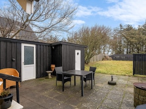 A patio area with a black metal shed, a white door, and a table with chairs. - 4 Star Holiday Home in Lokken (Lokken)