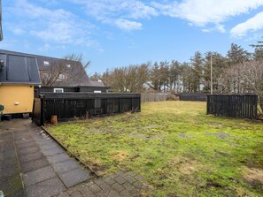 A residential backyard with a paved pathway, a fenced area, and a building with a dark roof. - 4 Star Holiday Home in Lokken (Lokken)