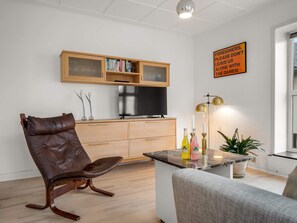 A modern living room with a leather chair, a flat-screen TV, wooden cabinets, and a dining area with a table and chairs. - 4 Star Holiday Home in Lokken (Lokken)