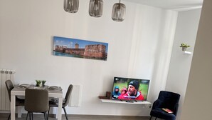 Un salon moderne comprenant un coin repas, un téléviseur et un tableau représentant un château.