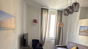 Un salon moderne comprenant un coin repas, un canapé, un téléviseur et une fenêtre avec des rideaux.