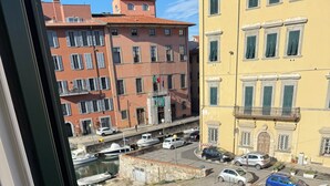 Une vue à travers une fenêtre sur une marina où des bateaux sont amarrés, avec des bâtiments en arrière-plan et un ciel dégagé.