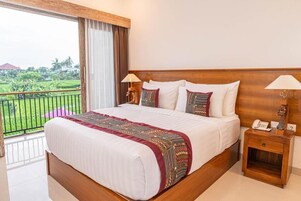 Habitación de hotel con una cama grande, dos mesitas de noche, un balcón con vistas a zonas verdes y un cabecero de madera.