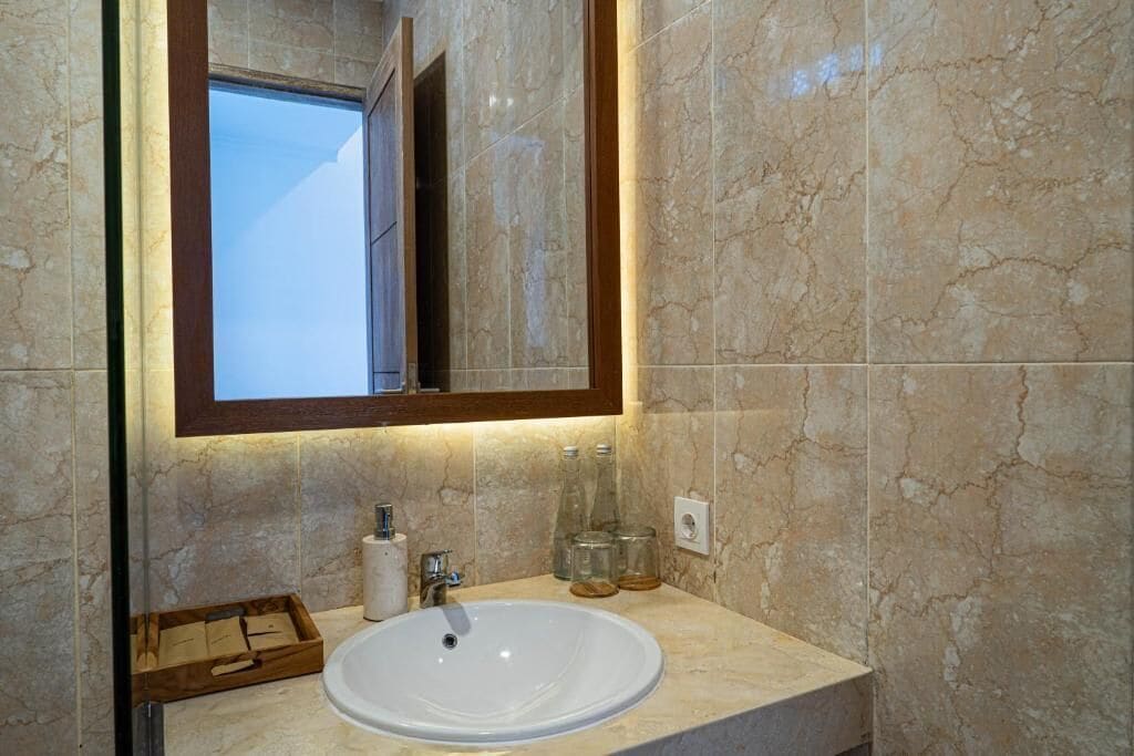 A bathroom with a marble sink, a mirror with a wooden frame, and a window.